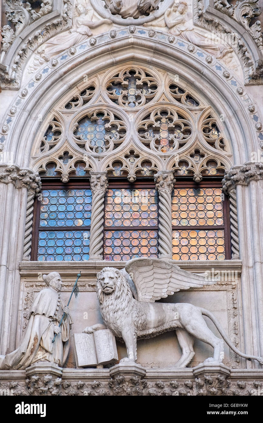 Statue of doge  and winged Lion on Doge's Palace facade with reflection of St Mark's campanile in the window's round glass tiles Stock Photo