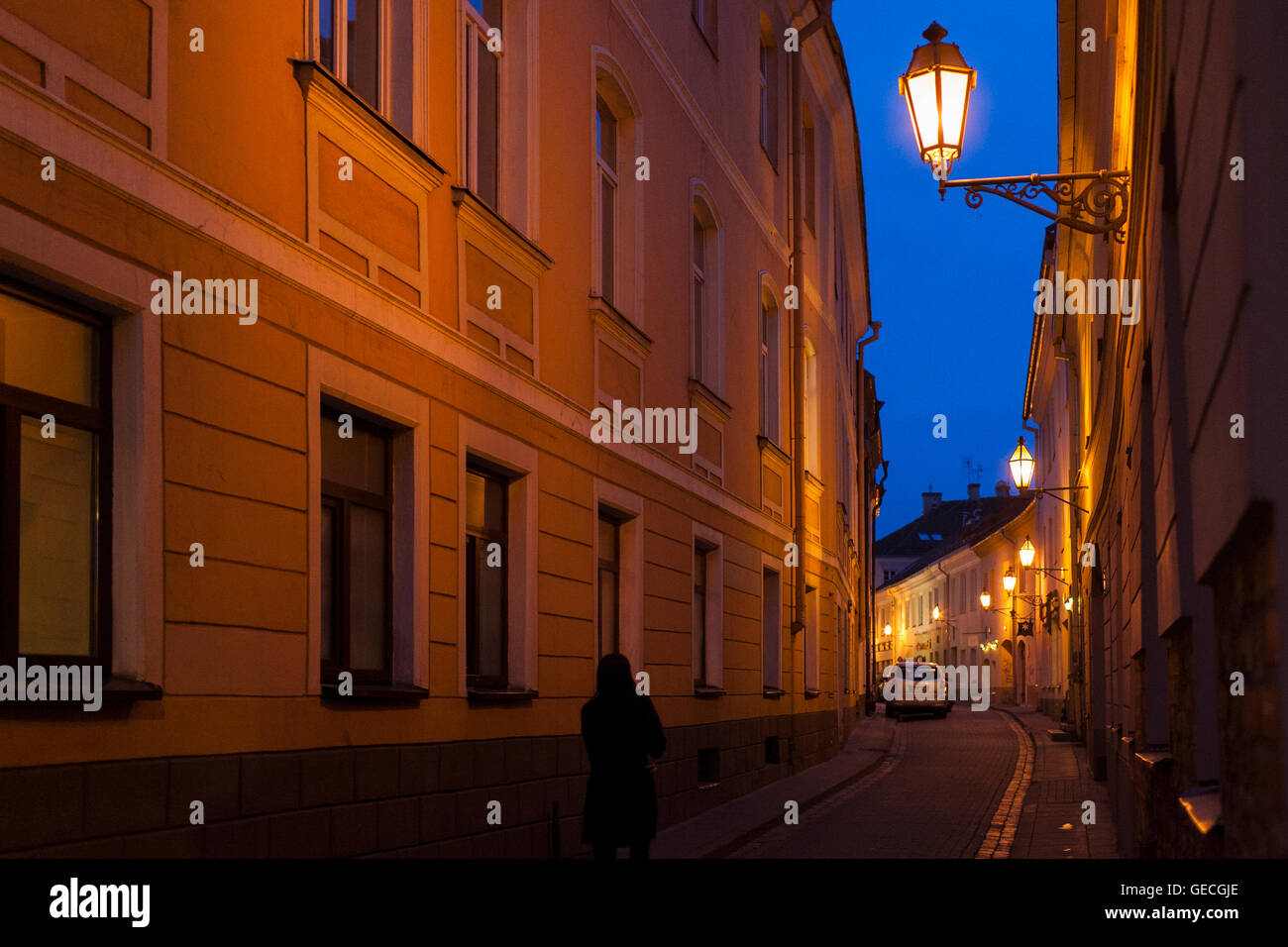 Walking down a twisting street past medieval architecture at night in the Lithuanian city of Vilnius Stock Photo