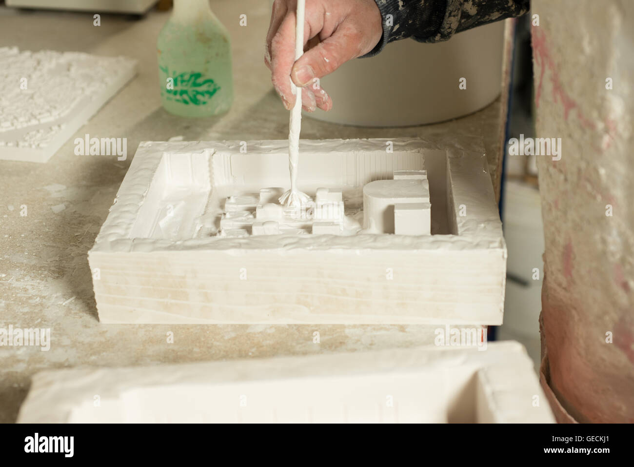 A hand applying a thin layer of plaster on rectangular mold using a