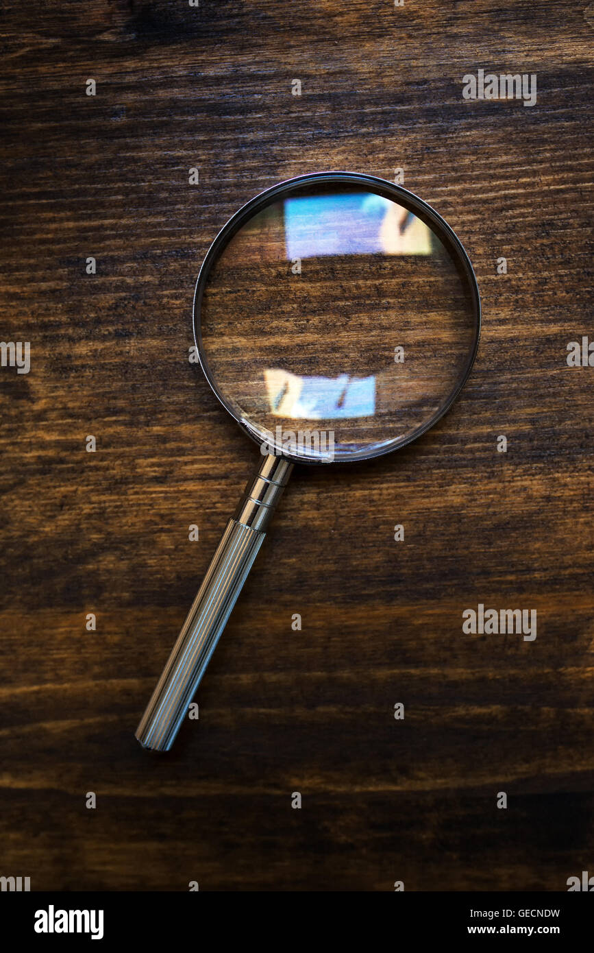 Loupe magnifying glass on wooden desk, top view, concept of searching and investigating Stock Photo