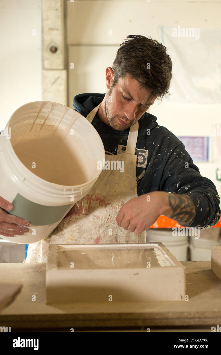 A man in plaster-splattered clothing and apron inspects freshly laid plaster on a rectangular mold Stock Photo