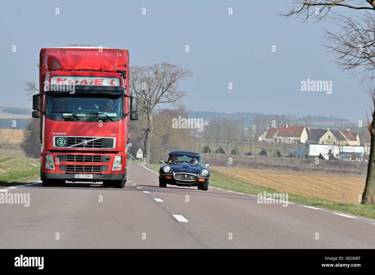Jaguar E-type classic car overtaking a large red articulated lorry on a clear road in the French countryside in Winter Stock Photo