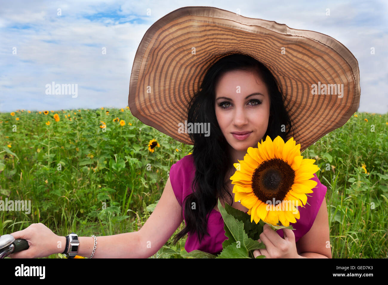 Pretty young brunette woman wearing large hat and sitting on bike in a ...