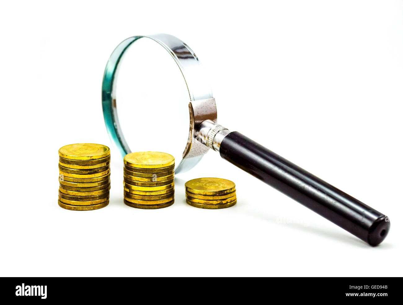 Gold Coins in front of magnifying glass in white background Stock Photo