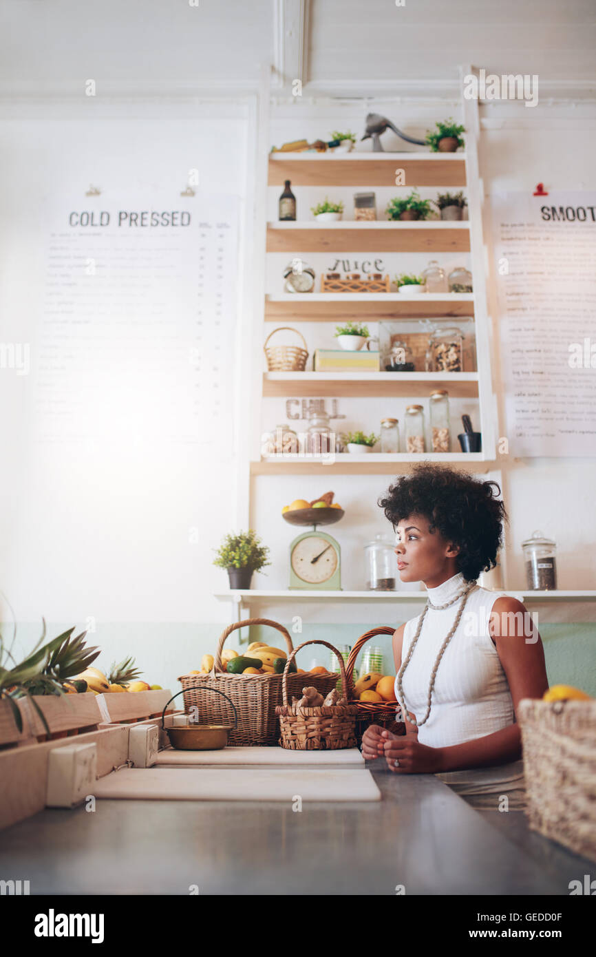 Side portrait of young woman behind juice bar counter. African woman standing and looking away. Stock Photo