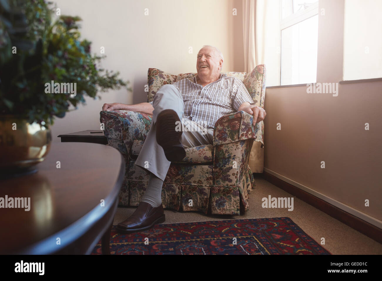 Indoor shot of smiling elderly man sitting on an arm chair at old age home. Stock Photo