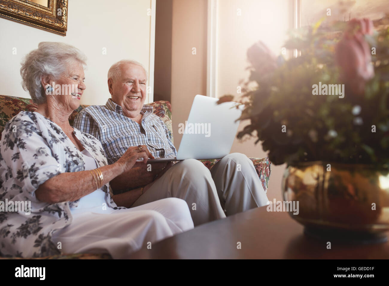 Portrait of smiling senior couple sitting together at home and surfing internet on laptop. Old man and woman relaxing on a sofa Stock Photo