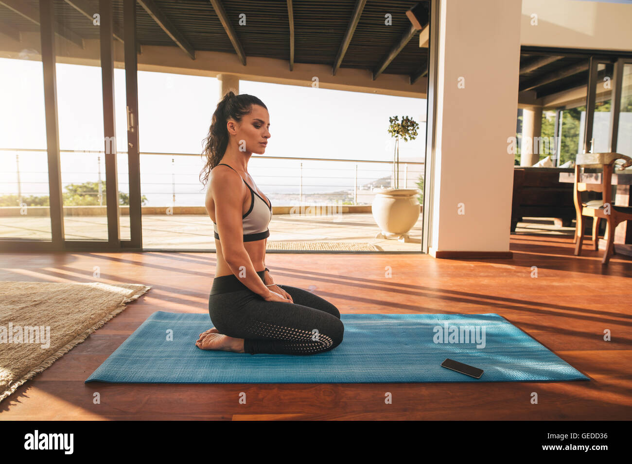 Side view shot of beautiful young woman sitting in yoga pose at home ...