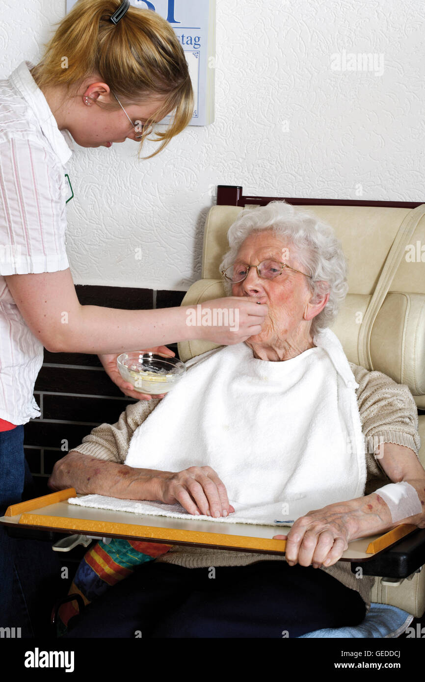 Caregiver feeding an elderly woman at a nursing home Stock Photo