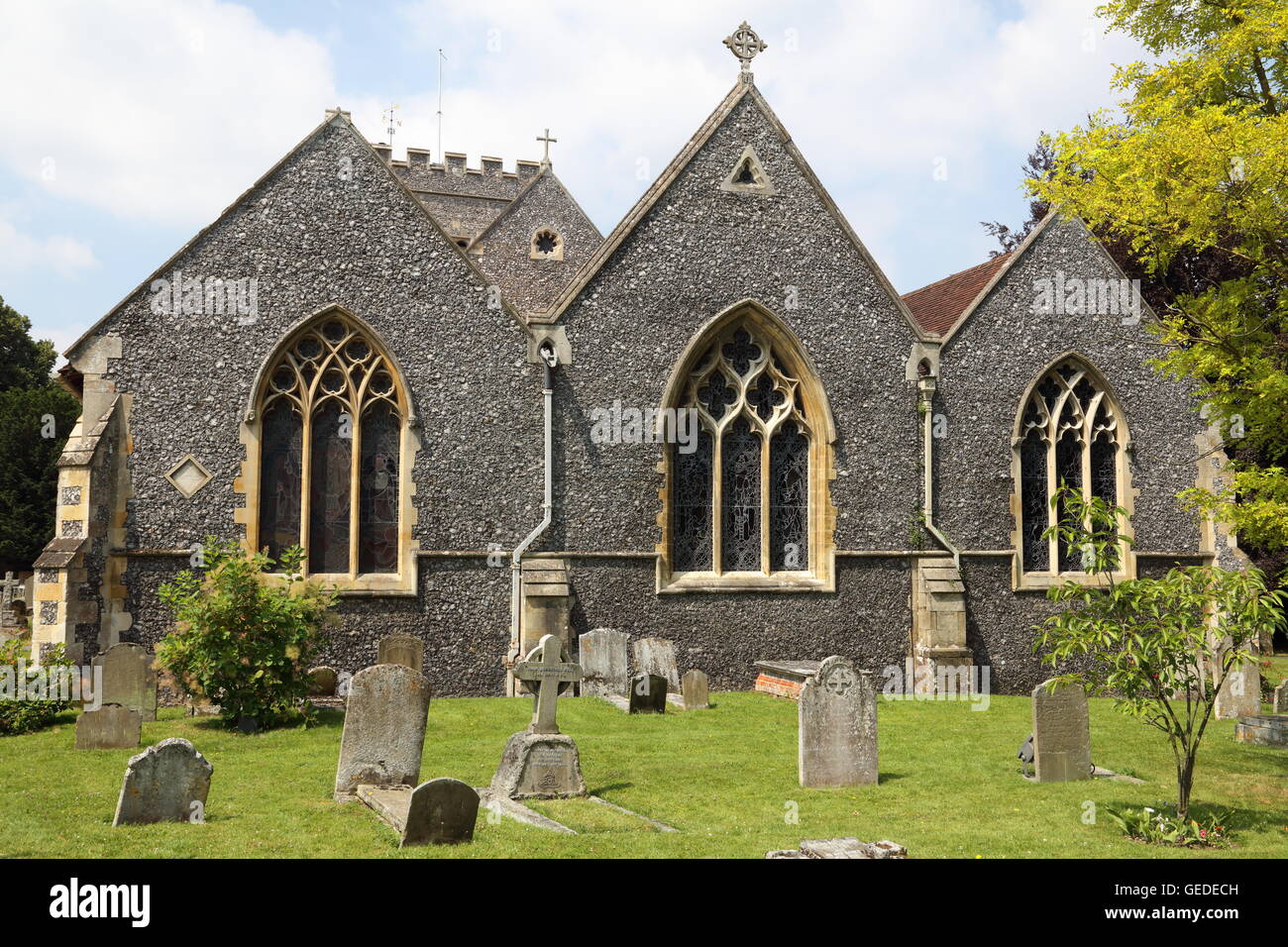 The East end of a local church with its leaded stained glass windows and a tower in the background and gravestones in the fore. Stock Photo