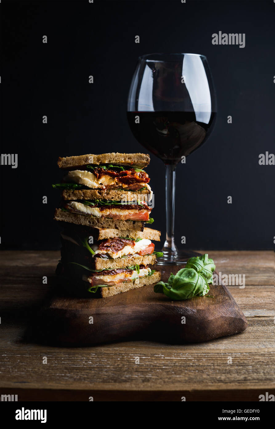 Caprese sandwich or panini and glass of red wine. Whole grain bread, mozzarella, dried tomatoes, basil. Dark background, vertical composition Stock Photo