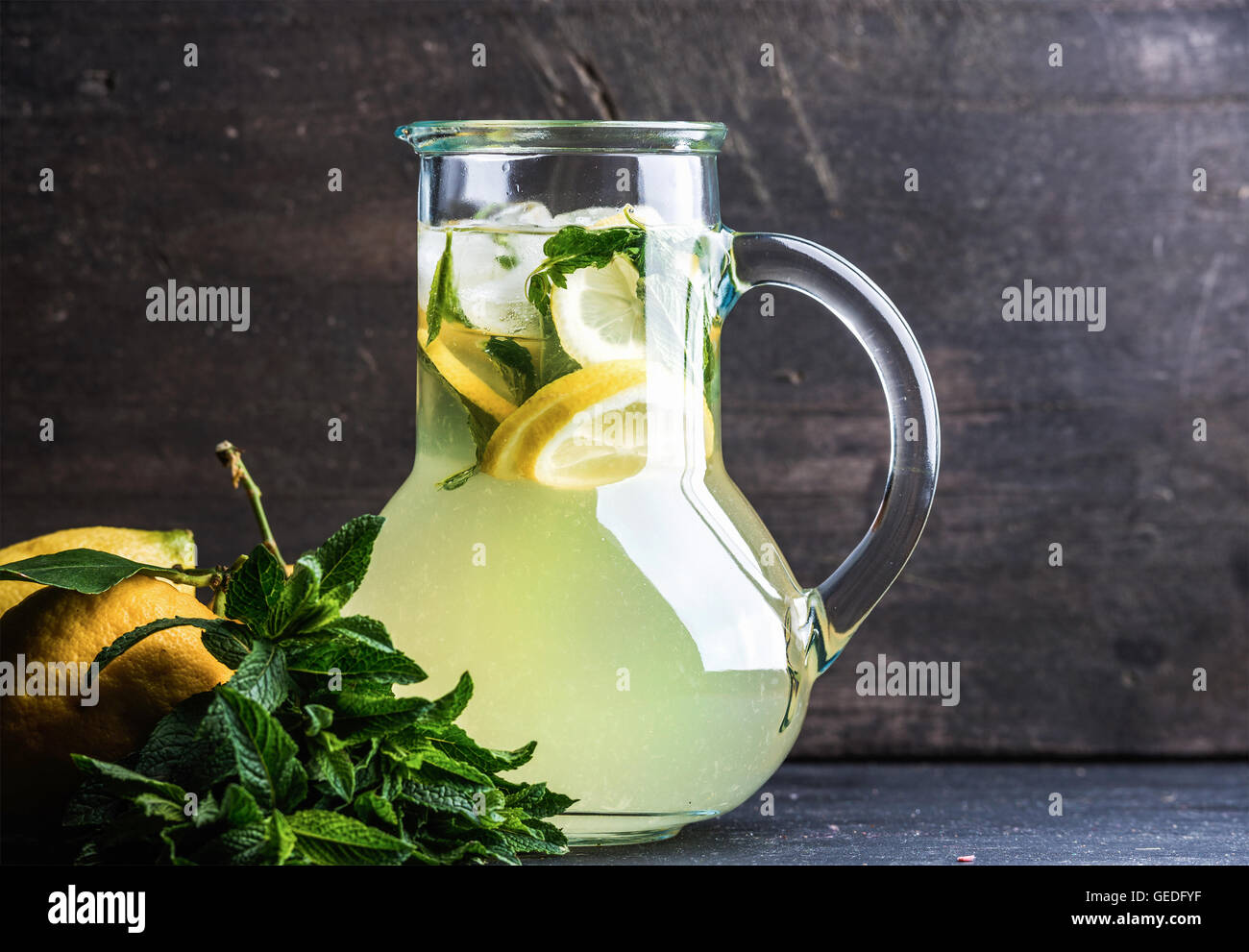 Homemade lemonade with mint, lemon slices and ice over dark background