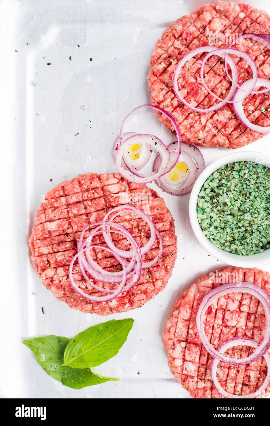 Three raw ground beef meat cutlets for making burgers with onion rings