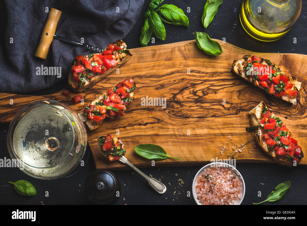 Tomato and basil bruschetta with glass of white wine, olive oil, salt, fresh herbs on wooden board over black background, copy space Stock Photo