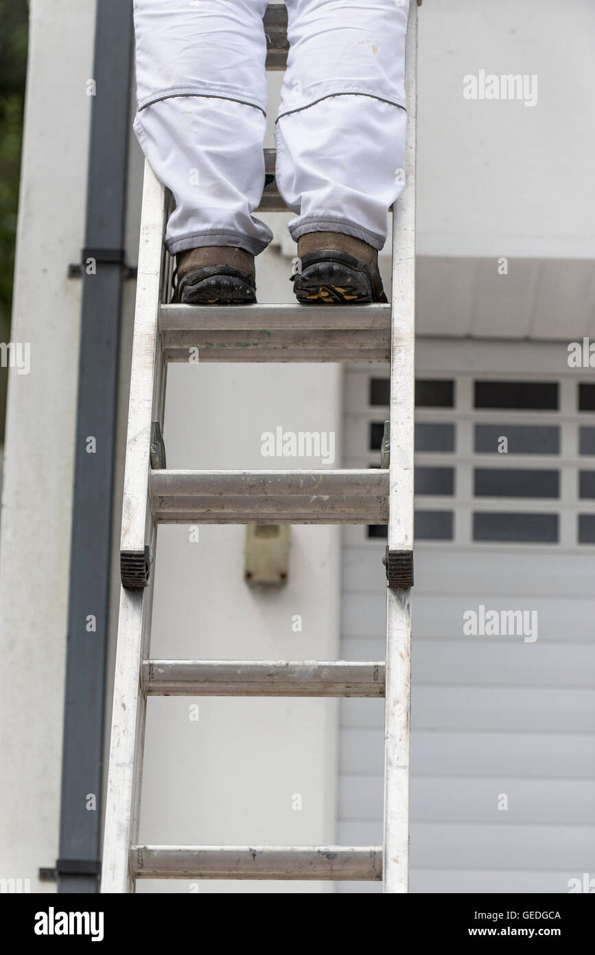 A painter and decorator stands on a ladder to paint the exterior wall of a house. Stock Photo