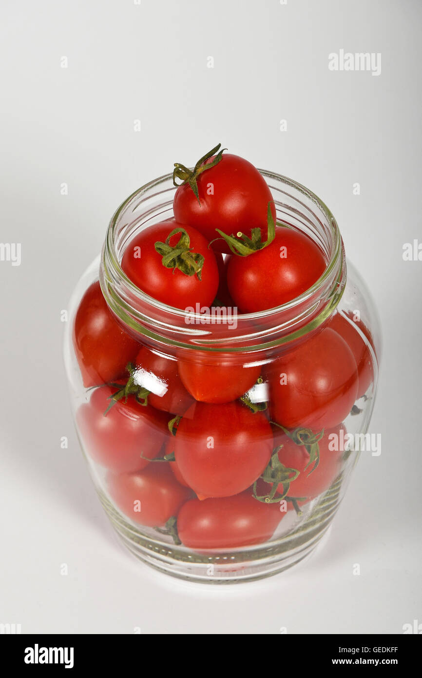 Glass jar full of red cherry tomatoes ready to pickle for conservation over white background, high angle view, close up Stock Photo