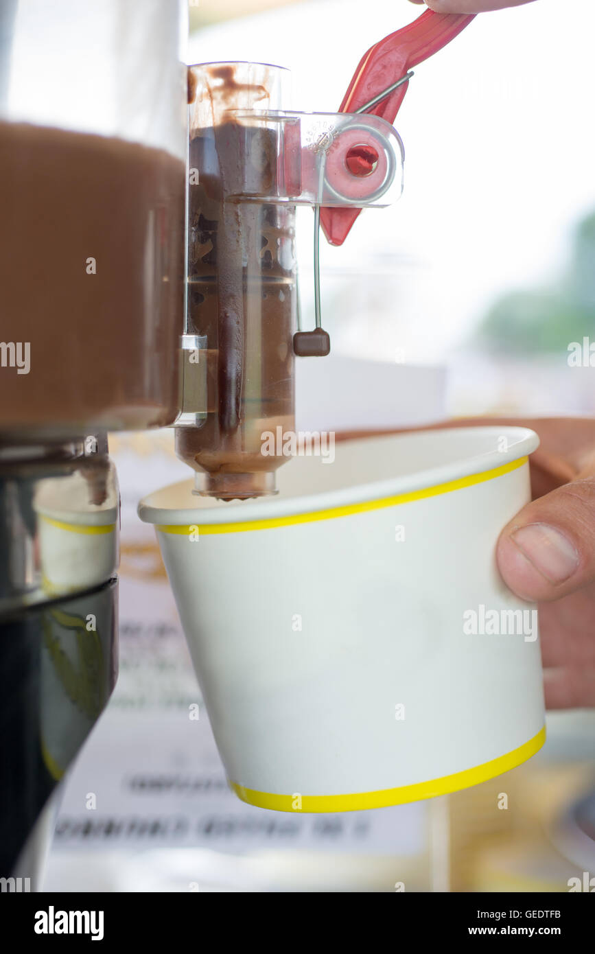 Close up shot of a mans hands holding a paper cup, filling it with chocolate dipping sauce from a pump at a churros stall Stock Photo