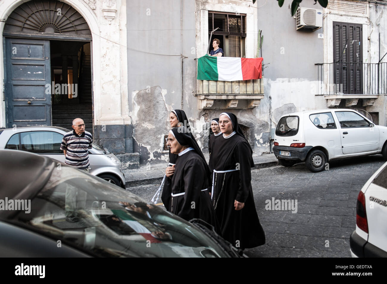 A man observe four nuns walking on a street of Catania, Sicily, while a woman stand on his balcony covered with an Italian flag. Stock Photo
