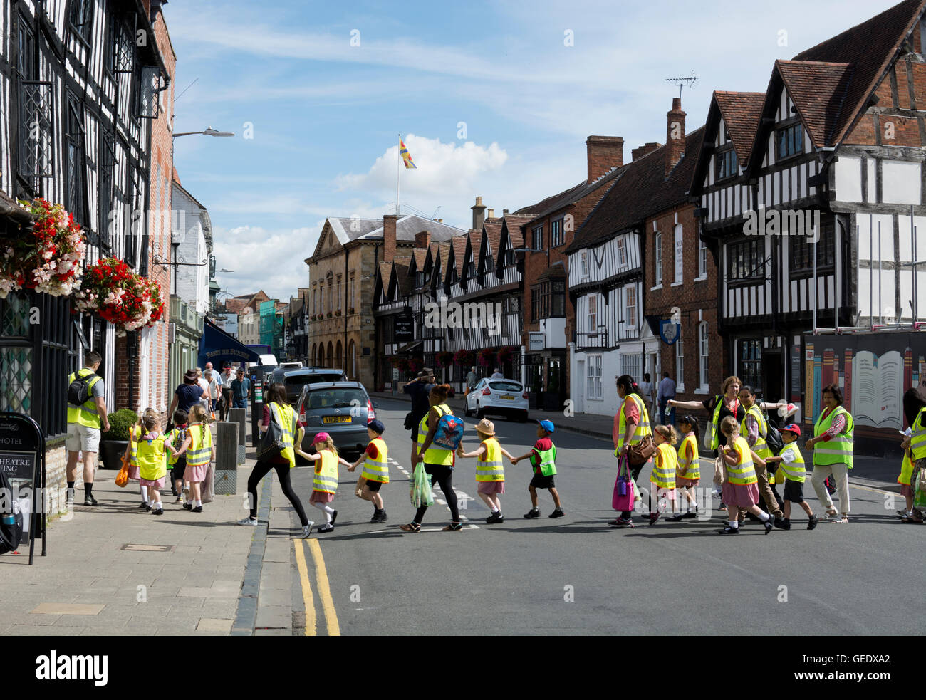 Children in high visibility waistcoats being led across a street, Stratford-upon-Avon, UK Stock Photo