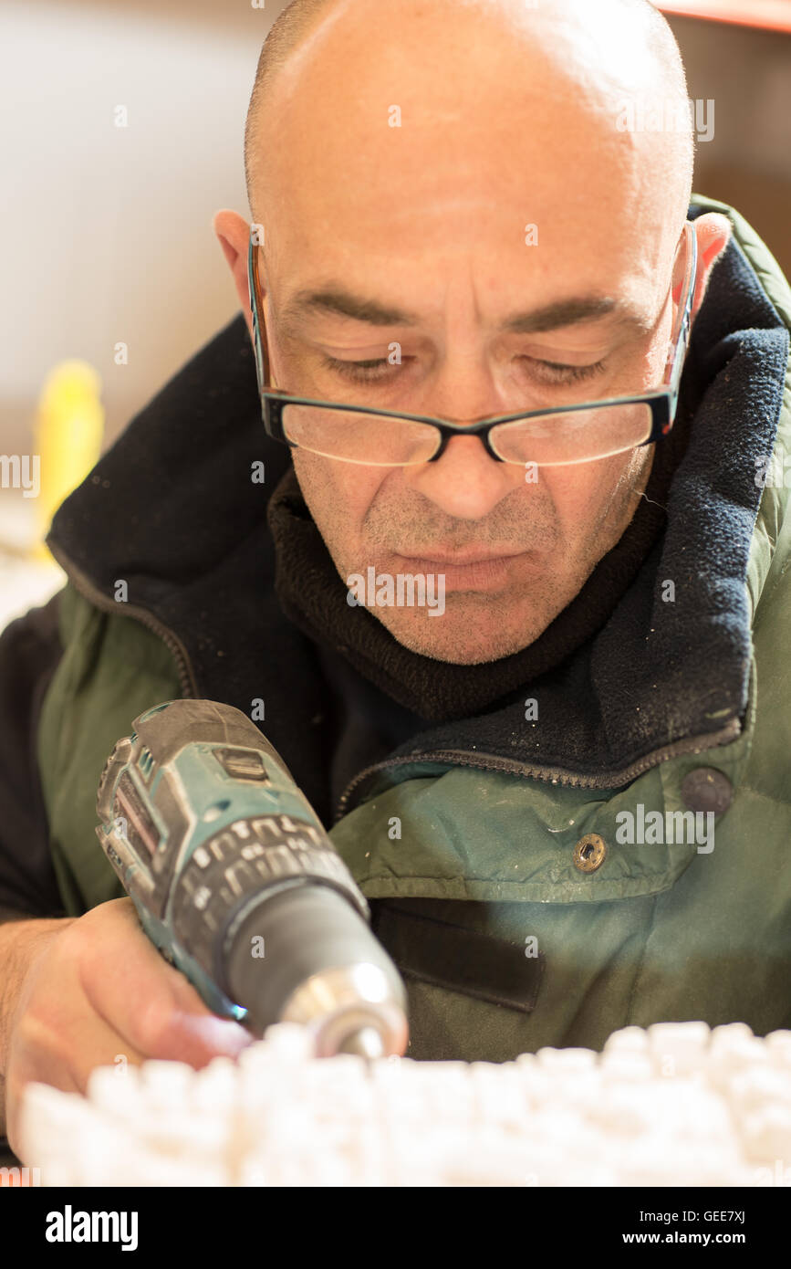 Man perforating a hole on the side of a plaster model using an electric drill. Stock Photo