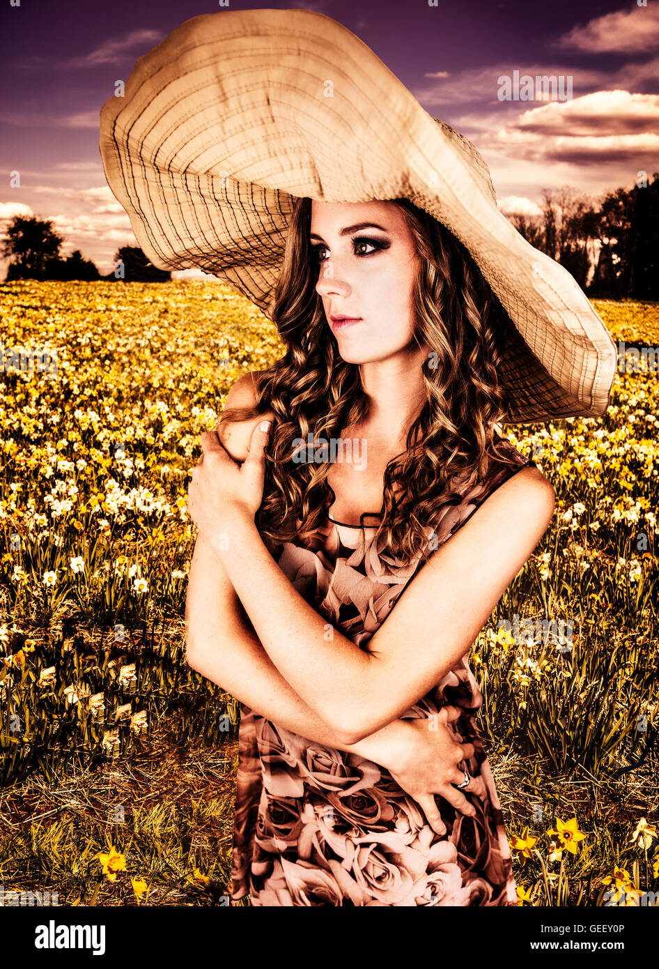 Beautiful young woman wearing big sun hat in a daffodil field Stock Photo