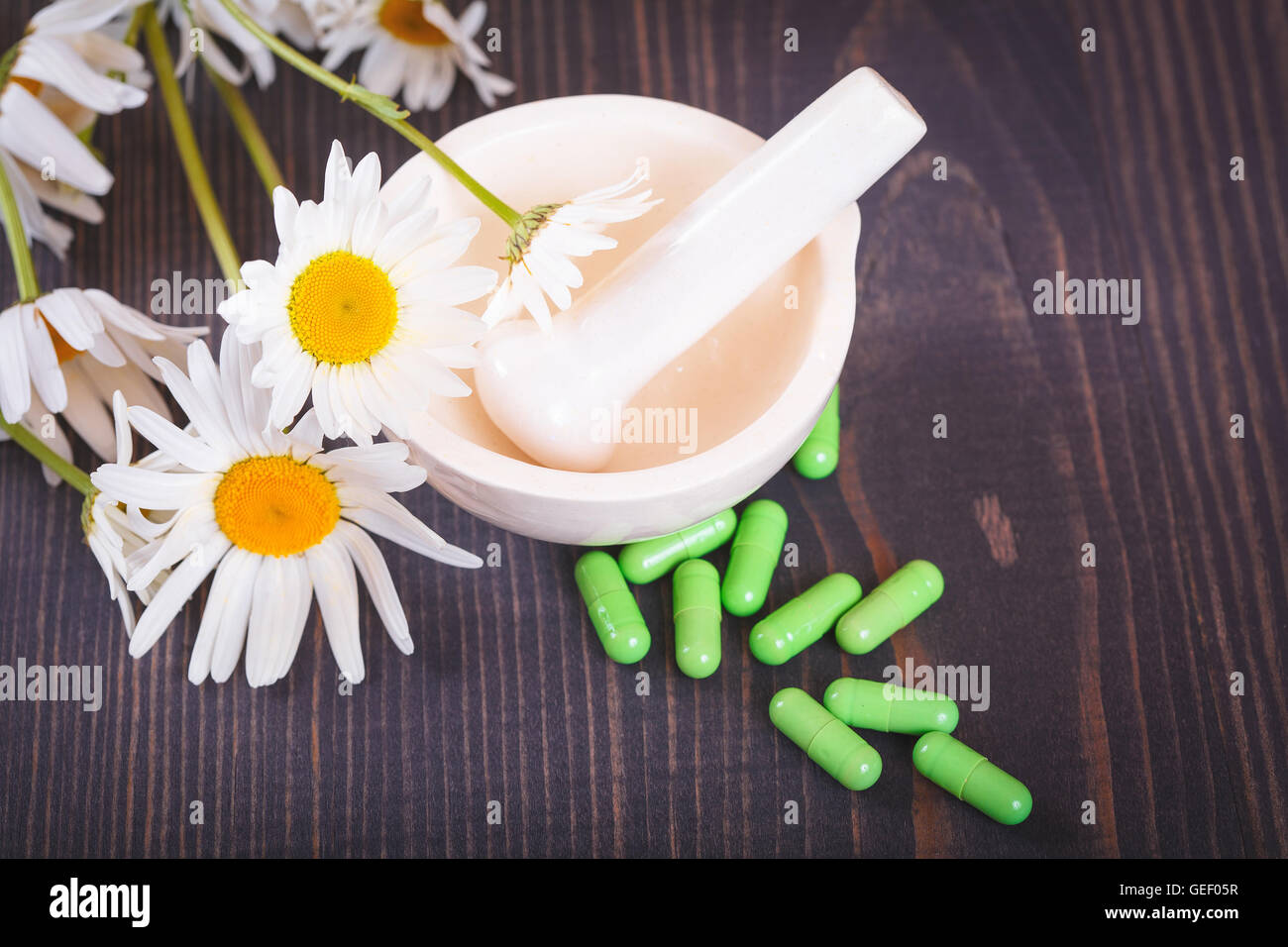 Chamomile flowers and green phytotherapeutic capsules on a wooden table. Herbal medicine and health Stock Photo