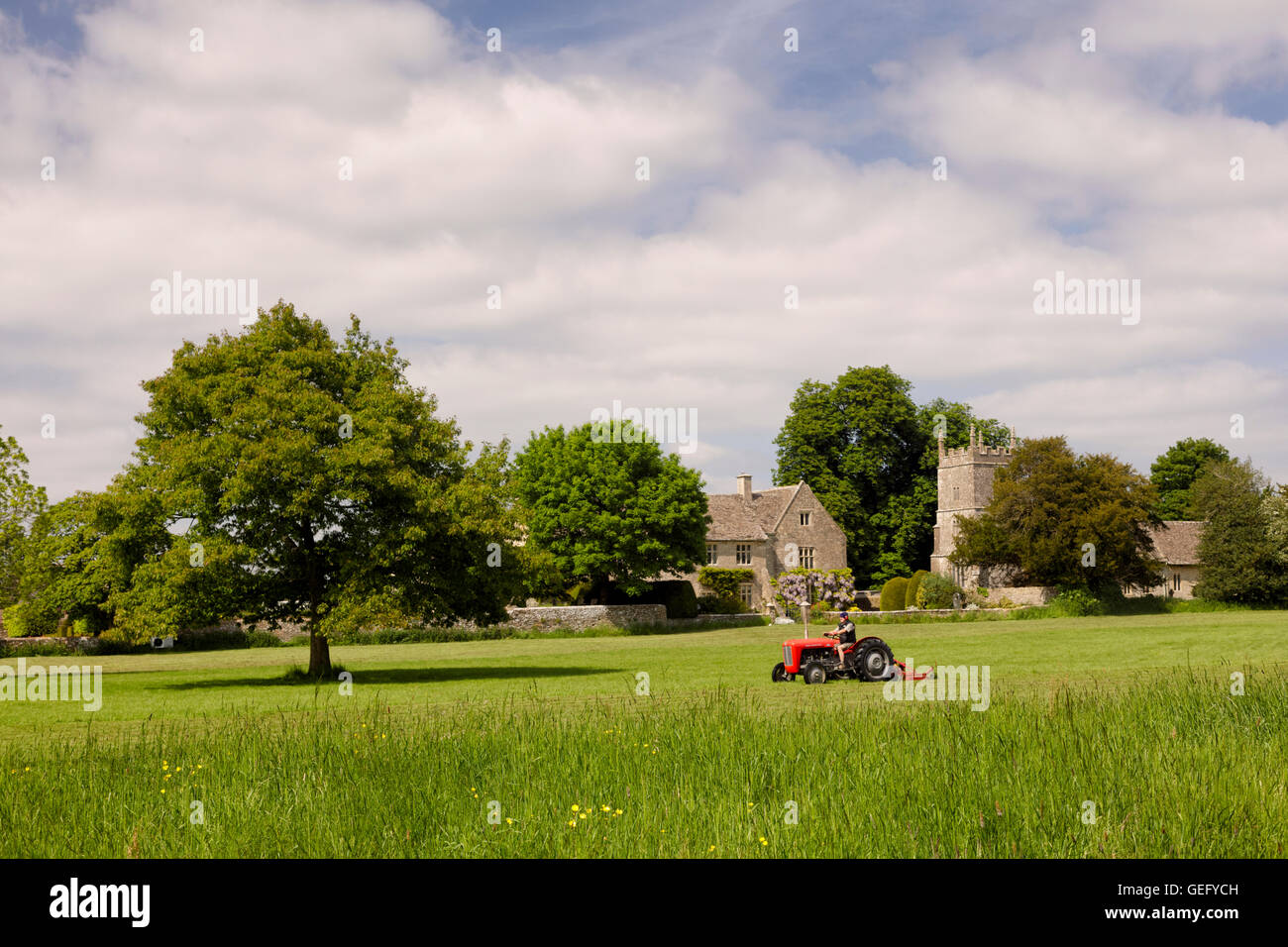 Red tractor cutting grass on a bright summer day near All Saints Church in Somerford Keynes Stock Photo