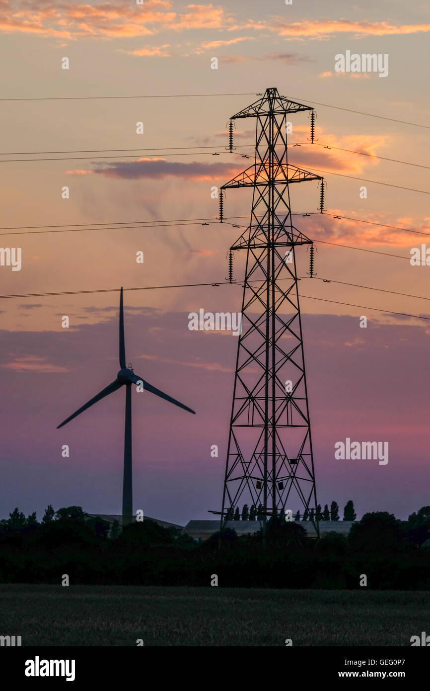 Wind turbine and electricity pylon side by side as the sun goes down in Norfolk Stock Photo
