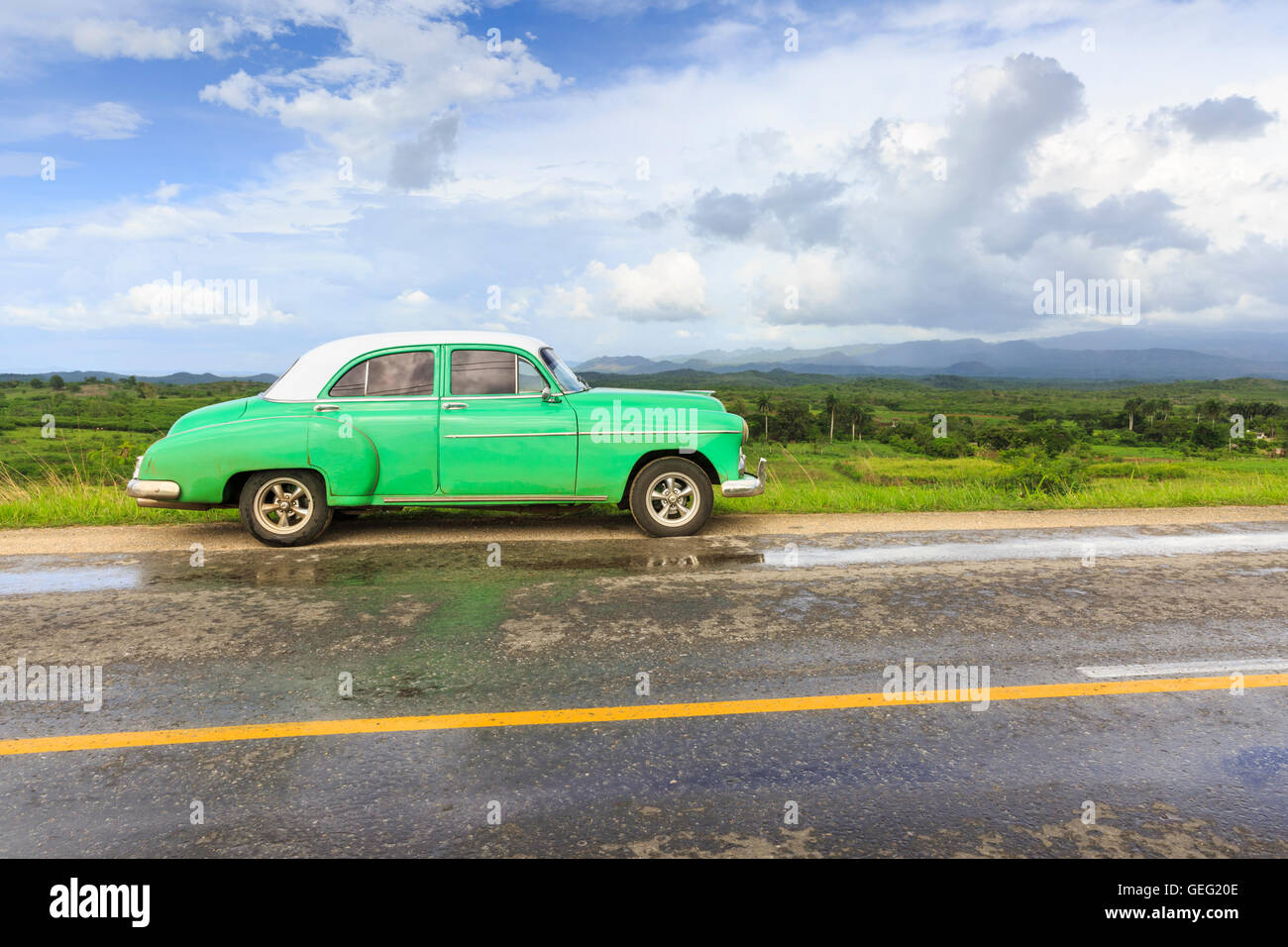 Old green classic car parked on the road in lush green countryside, Sancti Spiritus Province, Cuba Stock Photo