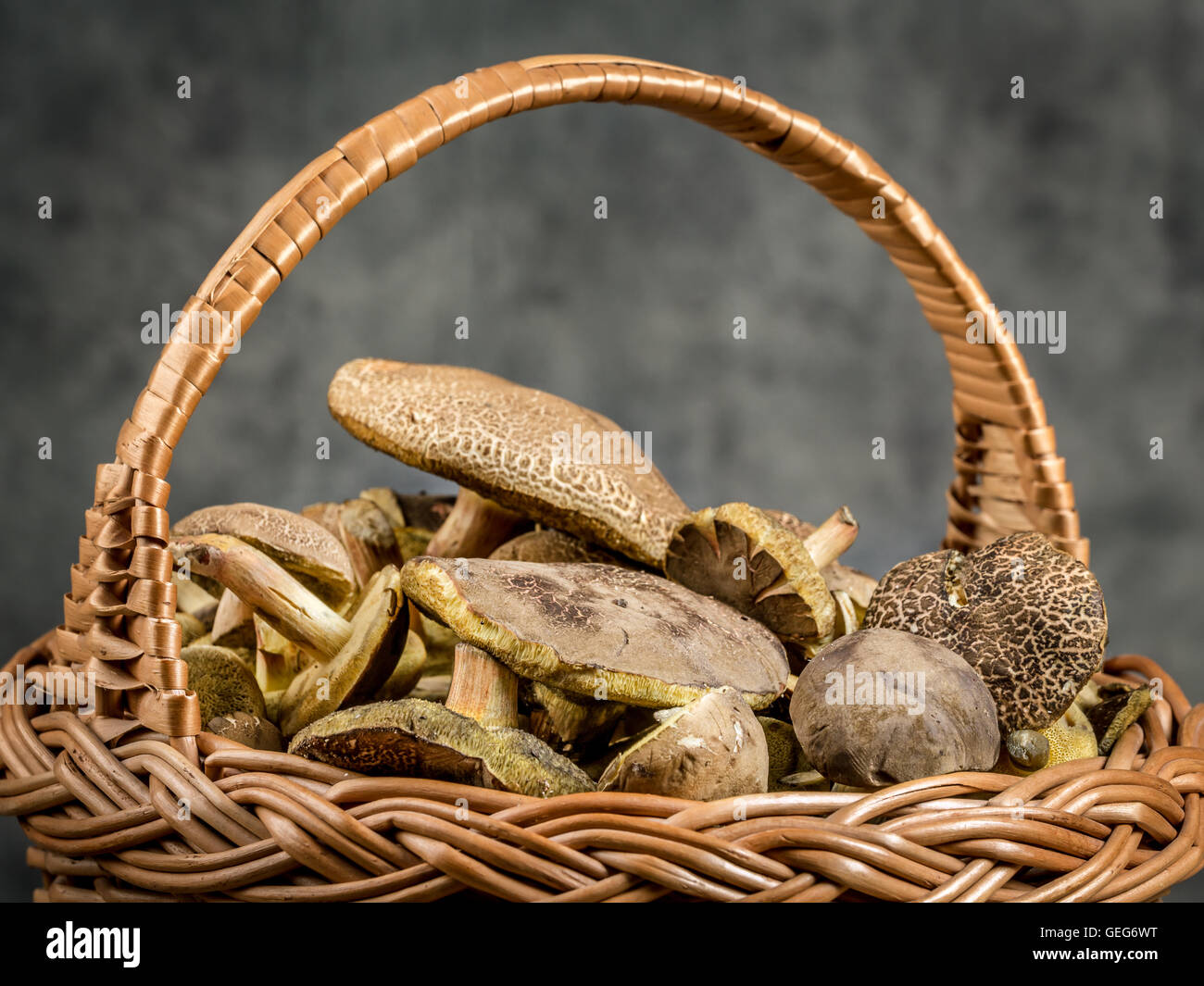 Wicker basket full of edible mushrooms on wooden table Stock Photo