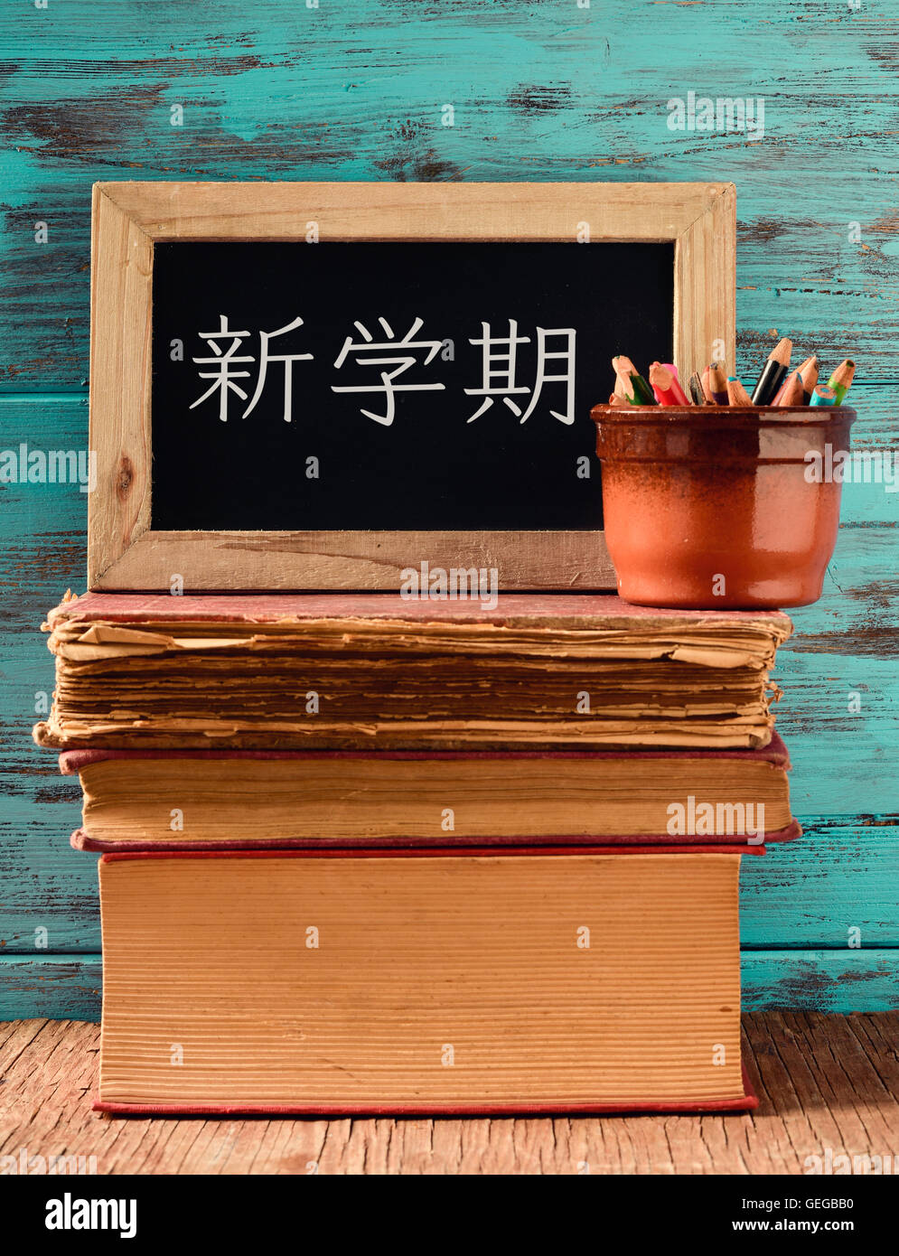 a chalkboard with the text back to school written in Japanese and a pot with some pencils on a pile of old books, placed on a ru Stock Photo