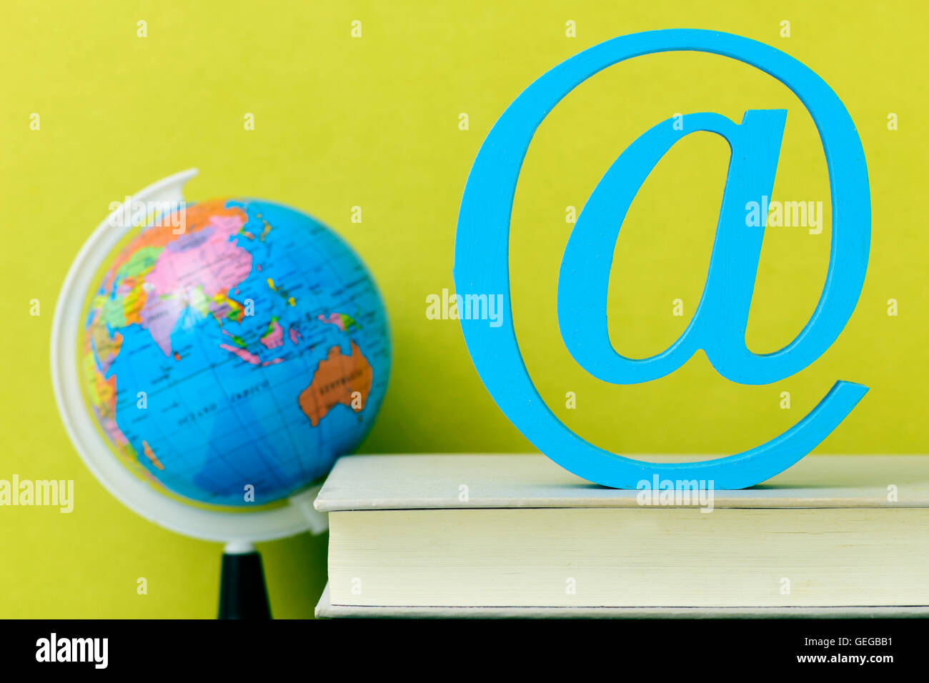 a three-dimensional blue at sign on a pile of books and a globe, depicting the concepts of the e-learning, the e-teaching, the d Stock Photo