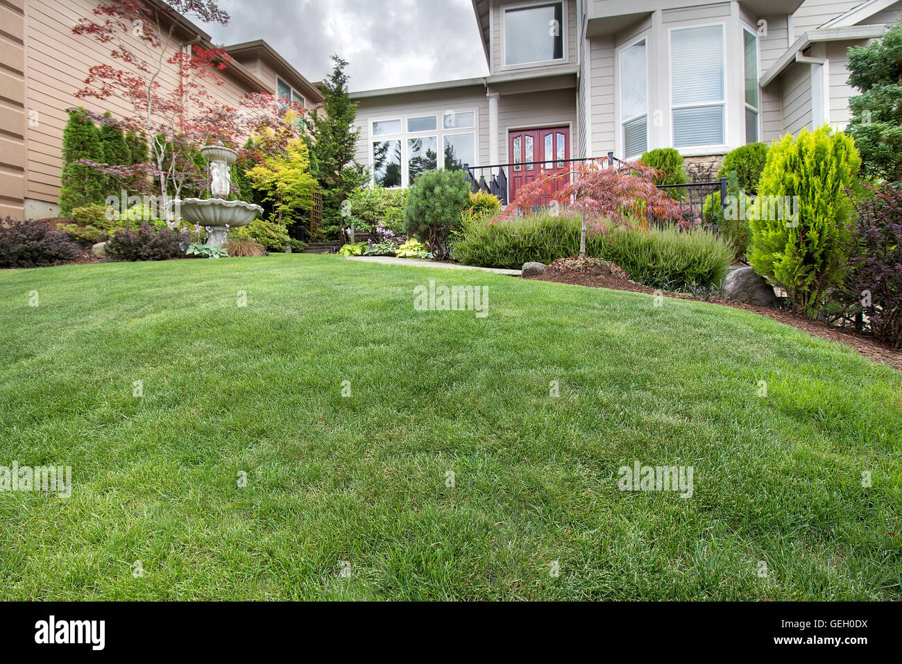 Green Grass Lawn in house front yard manicured garden with water fountain trees plant shrubs rocks in landscaping Stock Photo