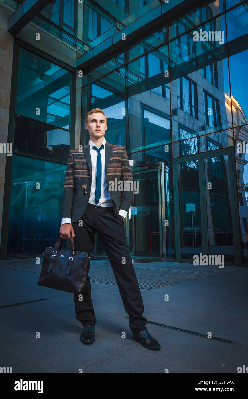 Young handsome successful stylish businessman standing near modern office building. Concept: victory. Stock Photo