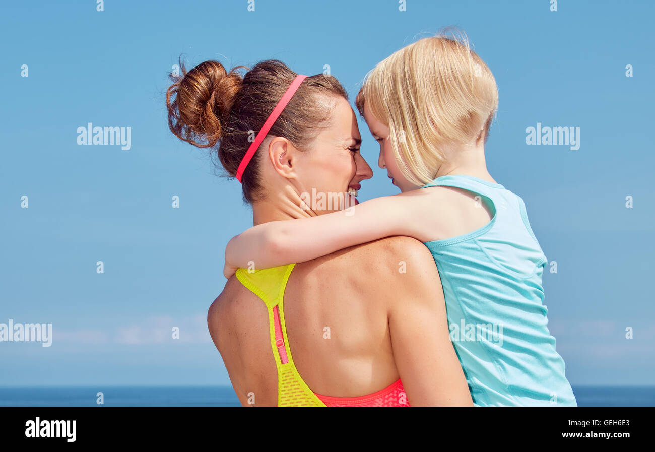 Look Good, Feel great! Seen from behind mother and child in fitness outfit hugging on embankment Stock Photo