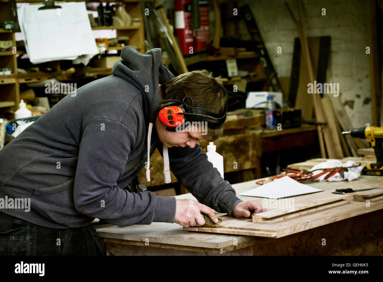 A man working in a furniture maker's workshop wearing ear defenders and using a sharp chisel on wood. Stock Photo