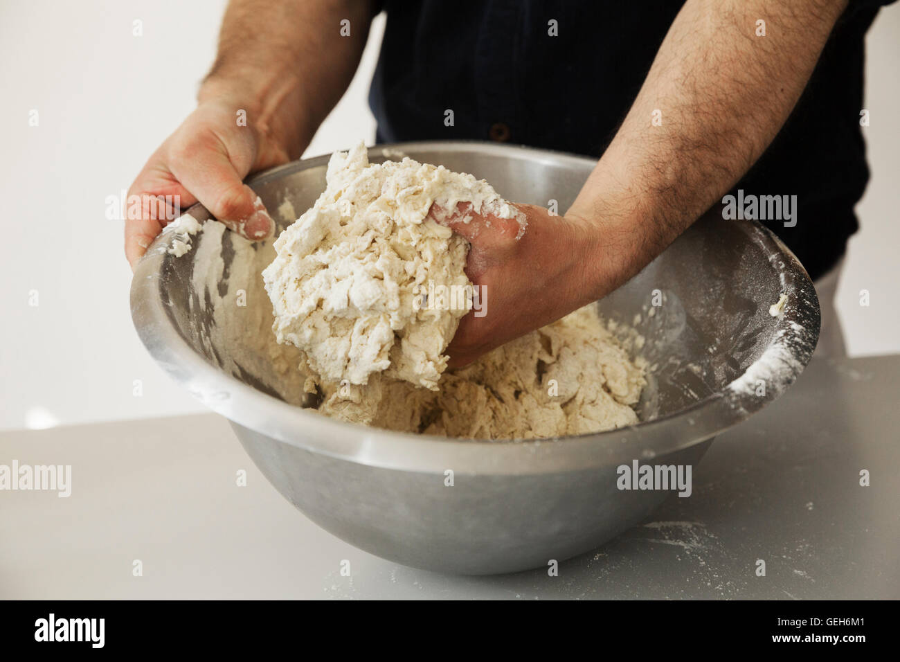 Close up of a baker kneading bread dough in a metal mixing bowl. Stock Photo