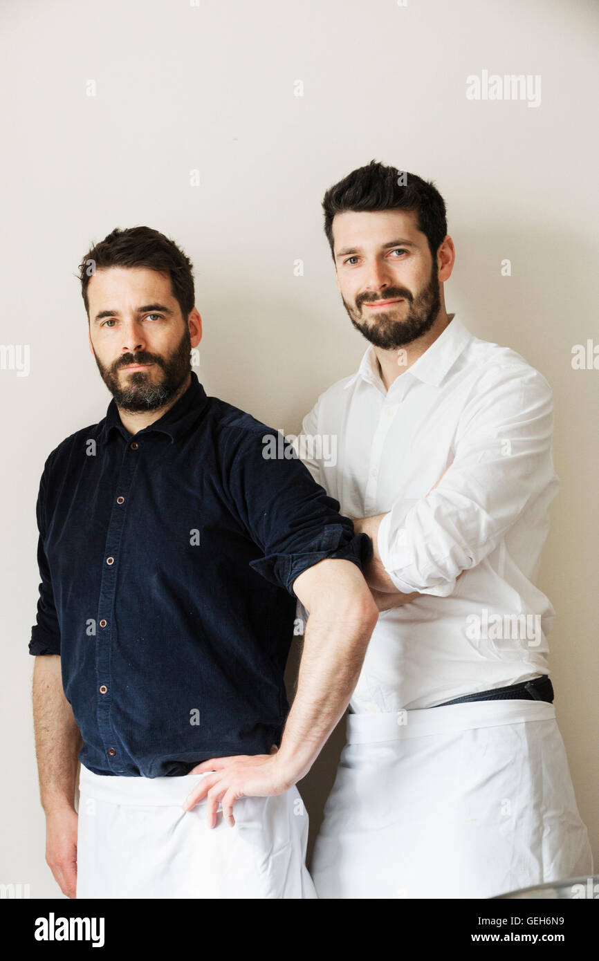 Half length portrait of two bearded men, wearing white aprons, looking at the camera. Stock Photo