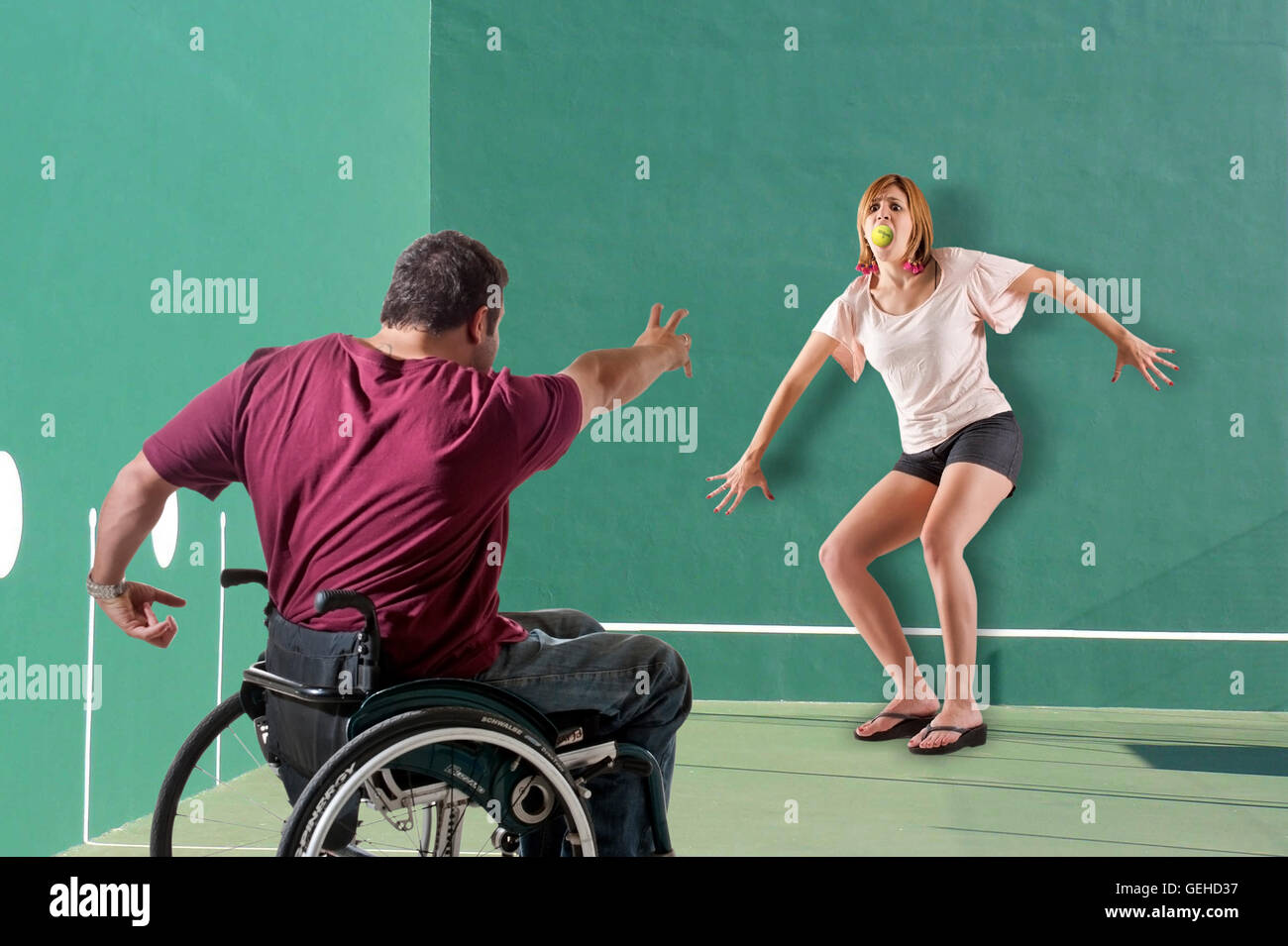 Man in a wheel chair throws a tennis ball into a woman's mouth Stock