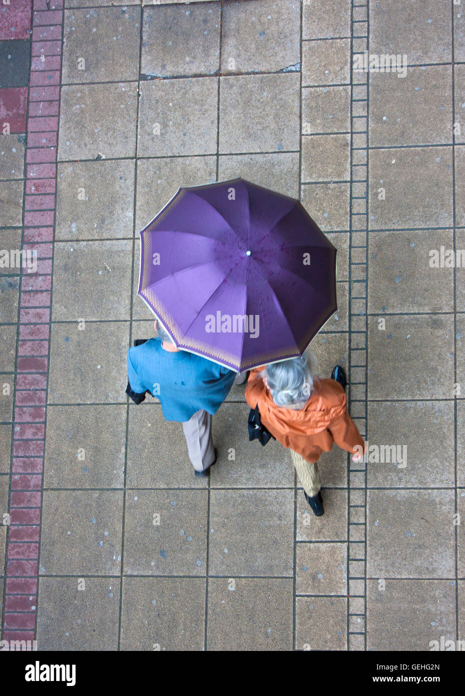 Senior couple sharing the umbrella while walking down the wet sidewalk in the center of Belgrade, Serbia, on May, 14th 2016. Dec Stock Photo