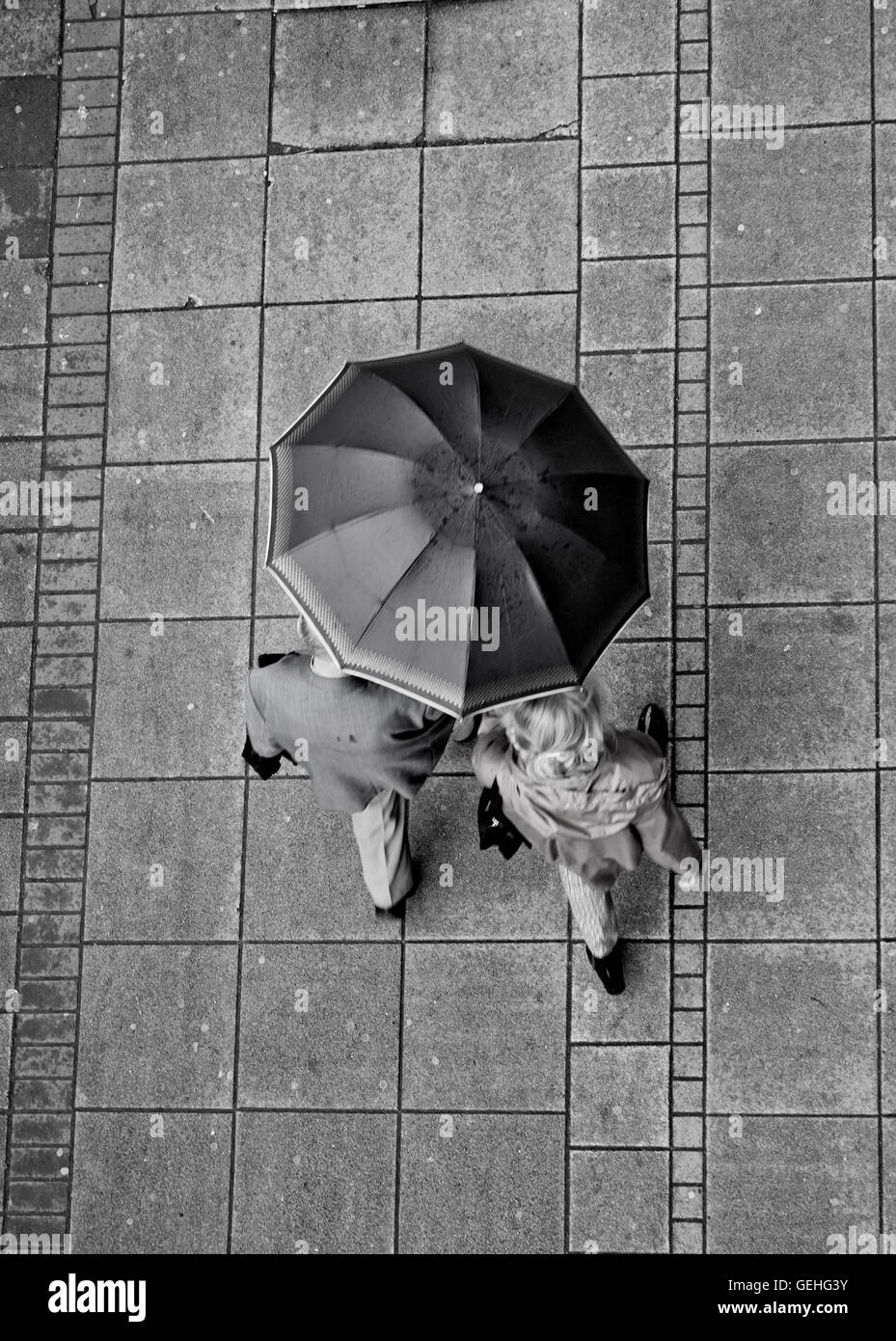 Couple sharing the umbrella while walking down the wet sidewalk in the center in black and white Stock Photo