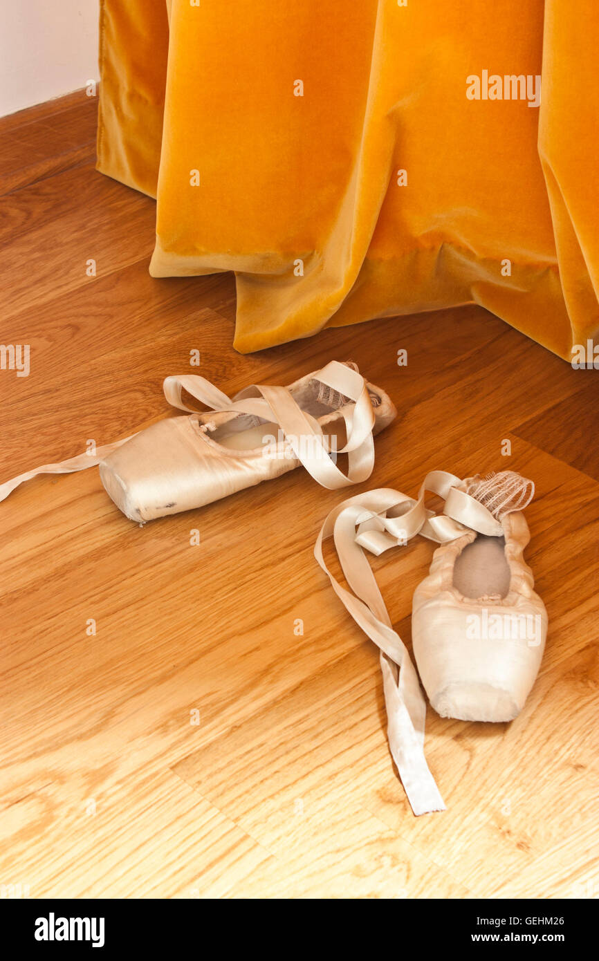 Pointe ballet shoes on the wooden floor in front of the orange curtain Stock Photo