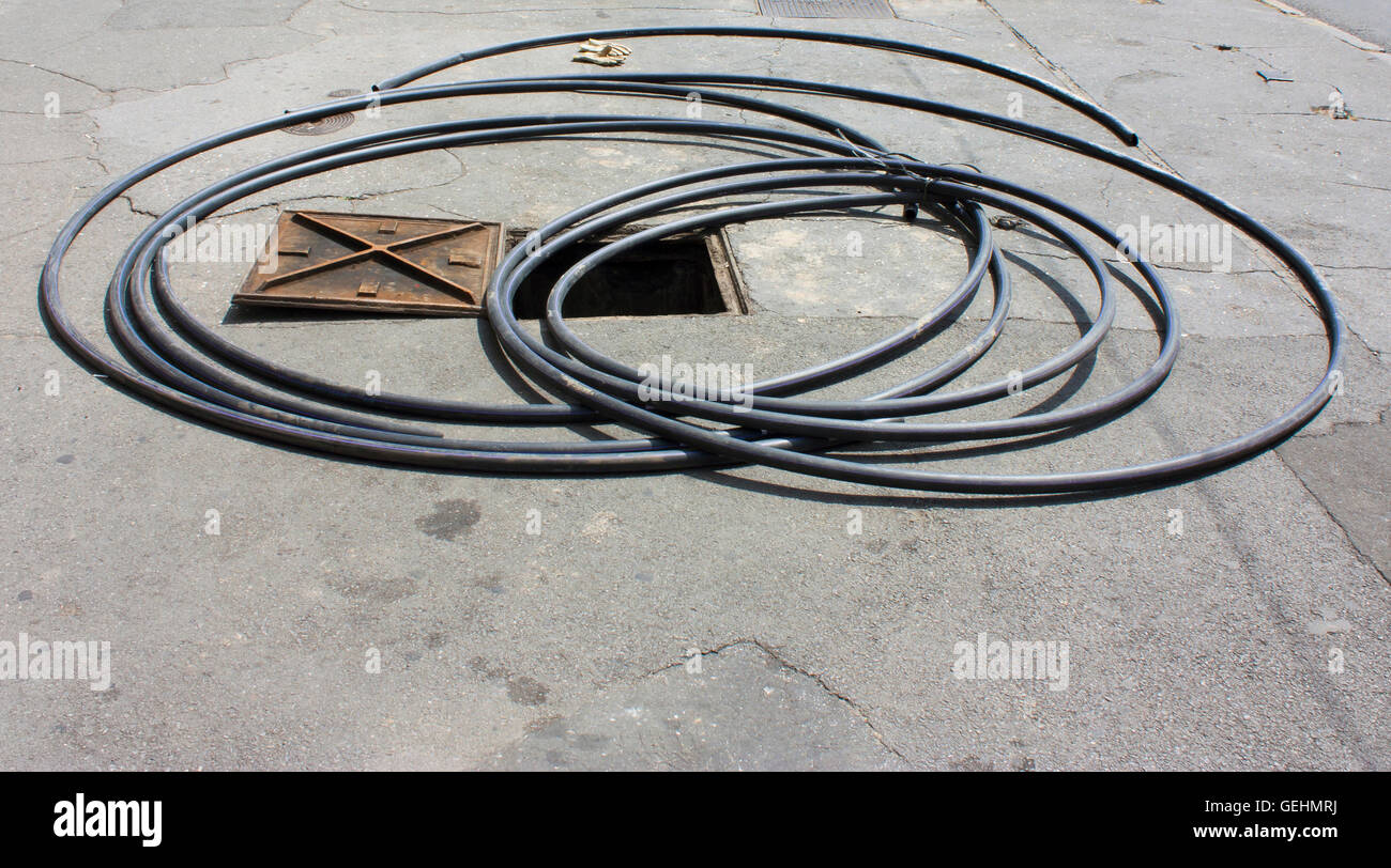 Long hose around open manhole and a pair of gloves Stock Photo