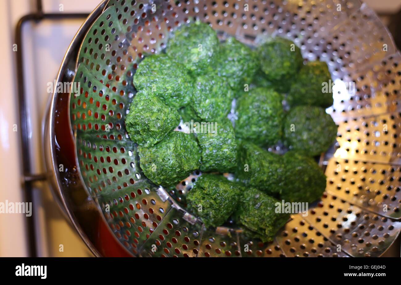 Steaming spinach. Steaming frozen chopped spinach in a steamer basket while brewing fresh tomatoes in the same pot. Stock Photo