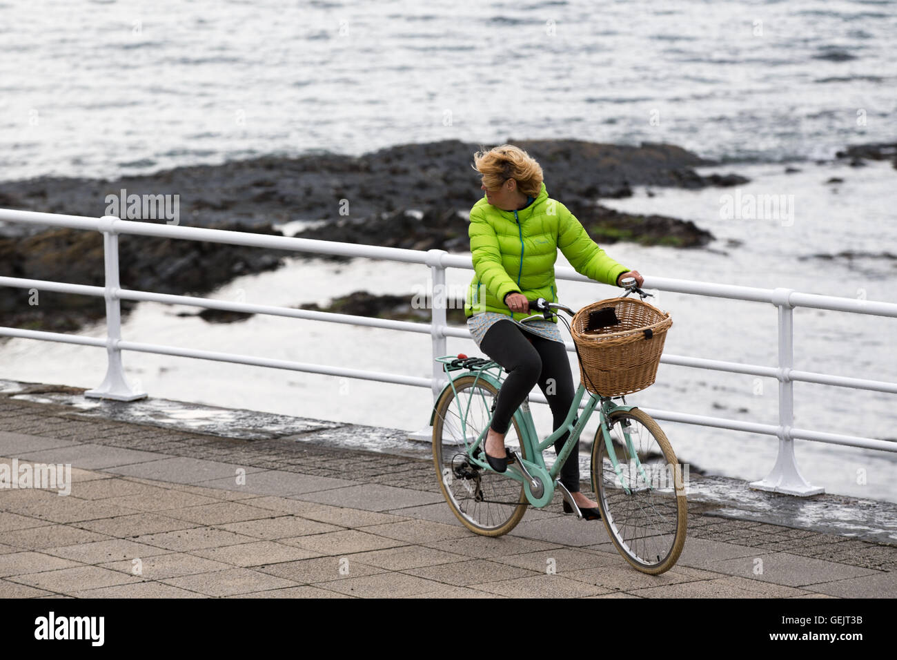 A woman looking over her shoulder as she rides a bicycle along the promenade Stock Photo