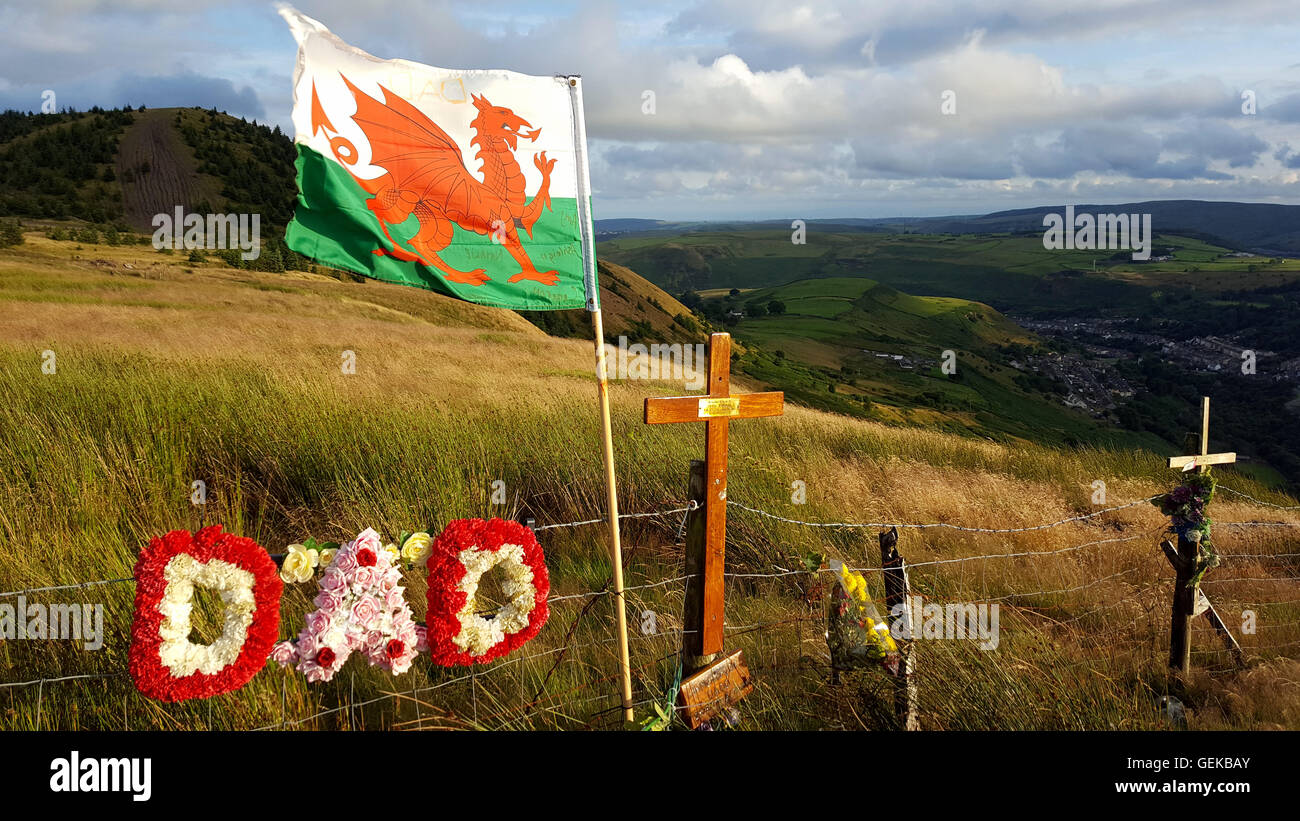 Rhondda Valley, Wales, UK. 25th July, 2016. The top of a windswept mountain in Wales has become a memorial to local peoples loved ones. A viewpoint over the Rhondda Valley high above the village of Blaenllechau has long been a place to stop and take in the views over the historic welsh valleys while driving over to the neighbouring Cynon Valley.  Locals have made the viewpoint somewhat of a shrine to lost loved ones and the recent addition of a welsh flag, maybe prompted by the wales football team’s success in the European football championships has made the site all the more dramatic. Stock Photo