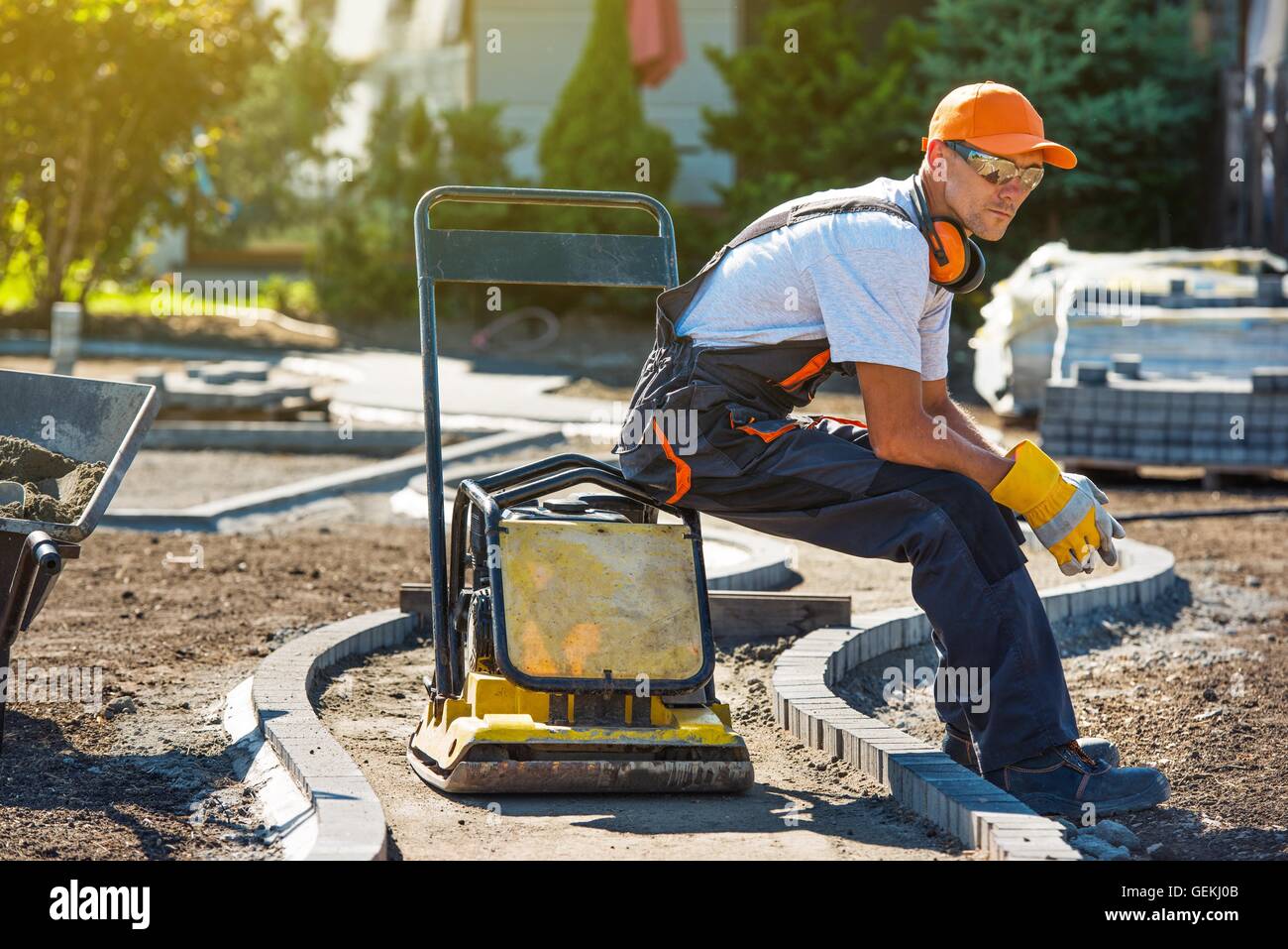 Brick Paver Worker Resting on His Soil Plate Compactor While at Work. Stock Photo