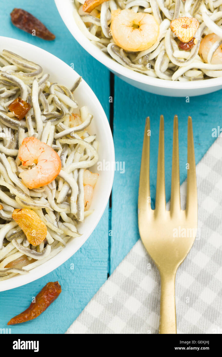 Surimi elvers with prawns, garlic and pepper on two white bowls, with a golden fork on a napkin Stock Photo