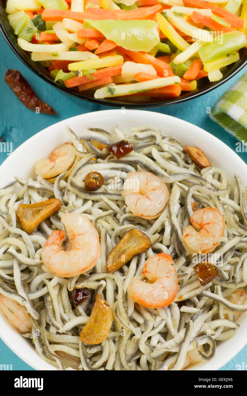 Surimi elvers with prawns, garlic and pepper on a white bowl, vegetables on a black bowl on a blue wooden table Stock Photo