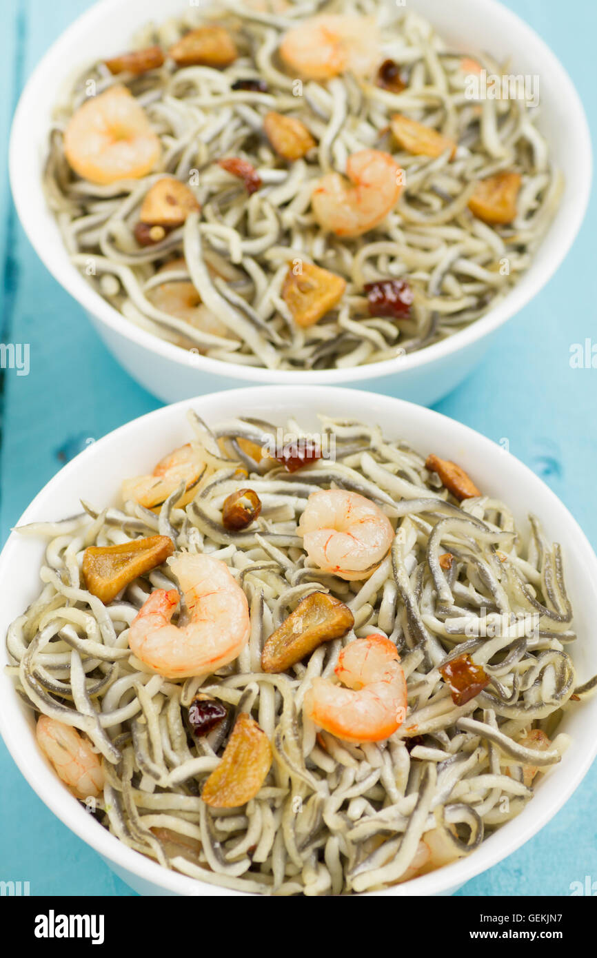 Surimi elvers with prawns, garlic and pepper on two white bowls on a blue wooden table Stock Photo